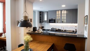 Een moderne keuken met grijze kastjes, een houten eettafel en een hangende hanglamp.