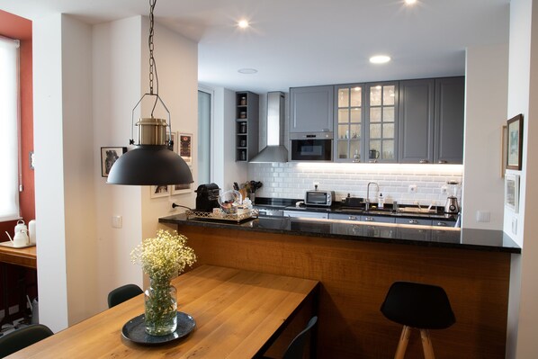 A modern kitchen with grey cabinets, a wooden dining table, and a hanging pendant light.