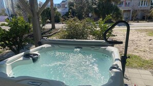 A hot tub with a pump and a bottle of oil on the side, surrounded by greenery and a paved area.