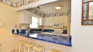 A kitchen with a blue countertop, white cabinets, a microwave, and four yellow stools.