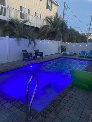 Piscina cercada por um muro branco, com palmeiras e cadeiras de descanso.