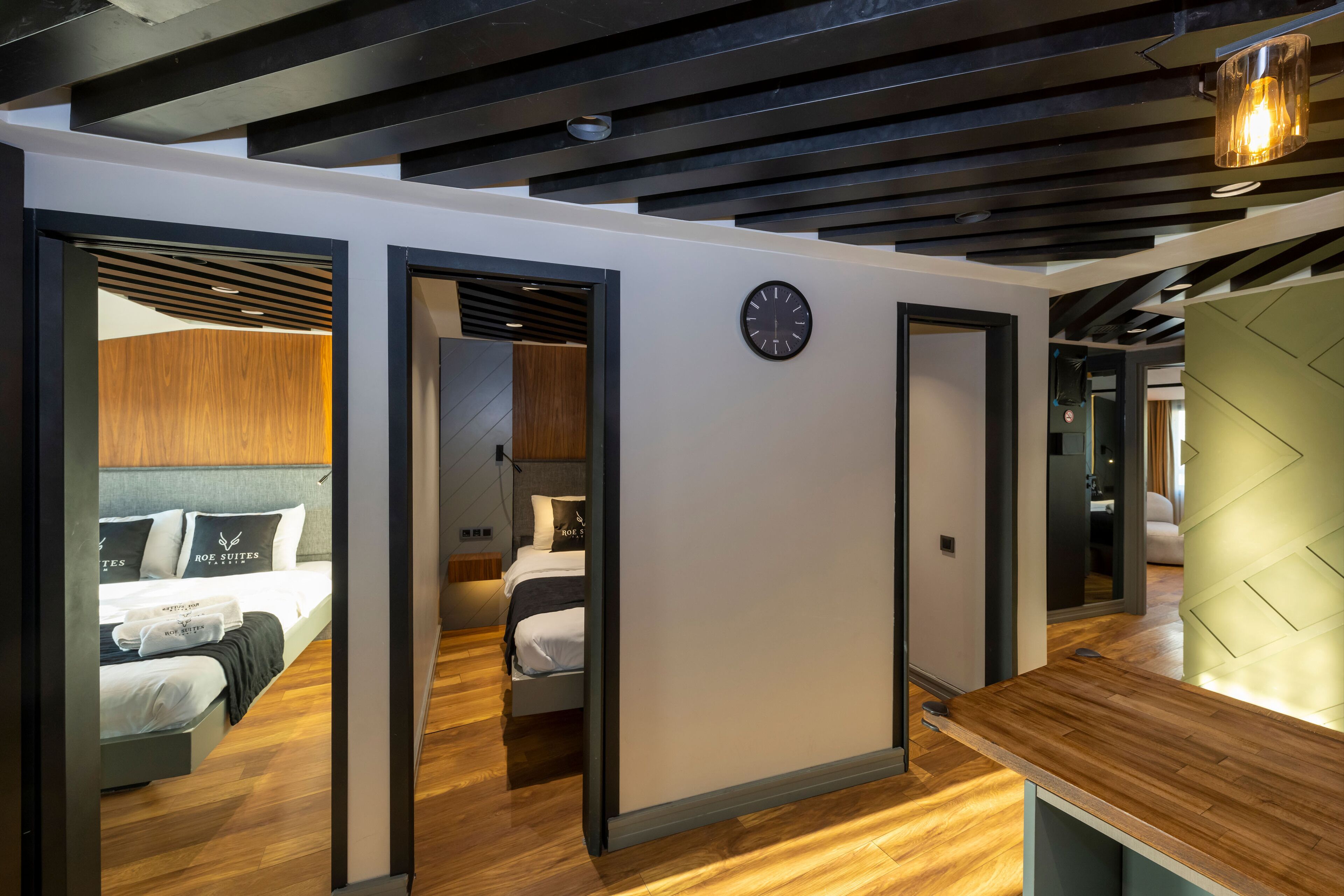 A modern hotel room with a wooden floor, a bed with white linens, a wall clock, and a green accent wall.