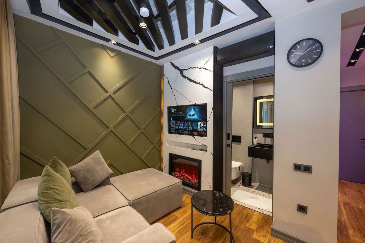 Ein modernes Wohnzimmer mit einer Couch, einem Kamin, einem Fernseher und einer Wanduhr.
