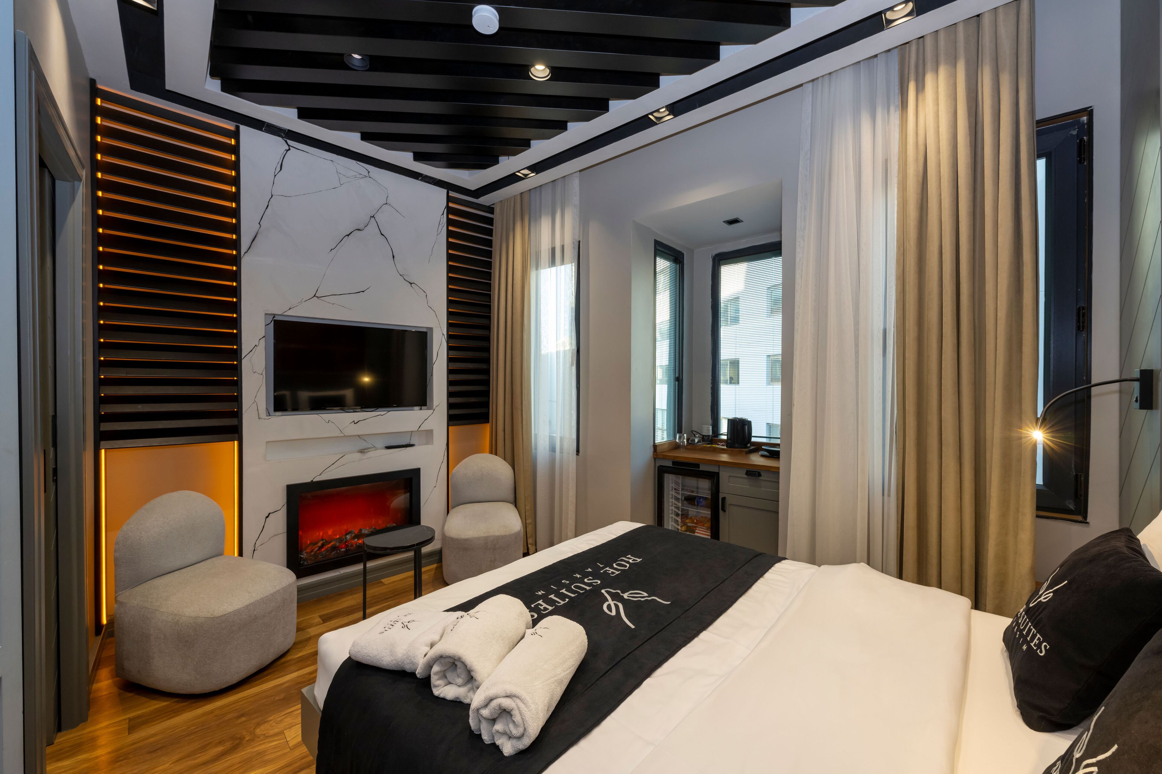 Une chambre d’hôtel moderne dotée d’un grand lit, d’un téléviseur à écran plat fixé au mur, d’un petit bureau et d’un coin salon avec un fauteuil.