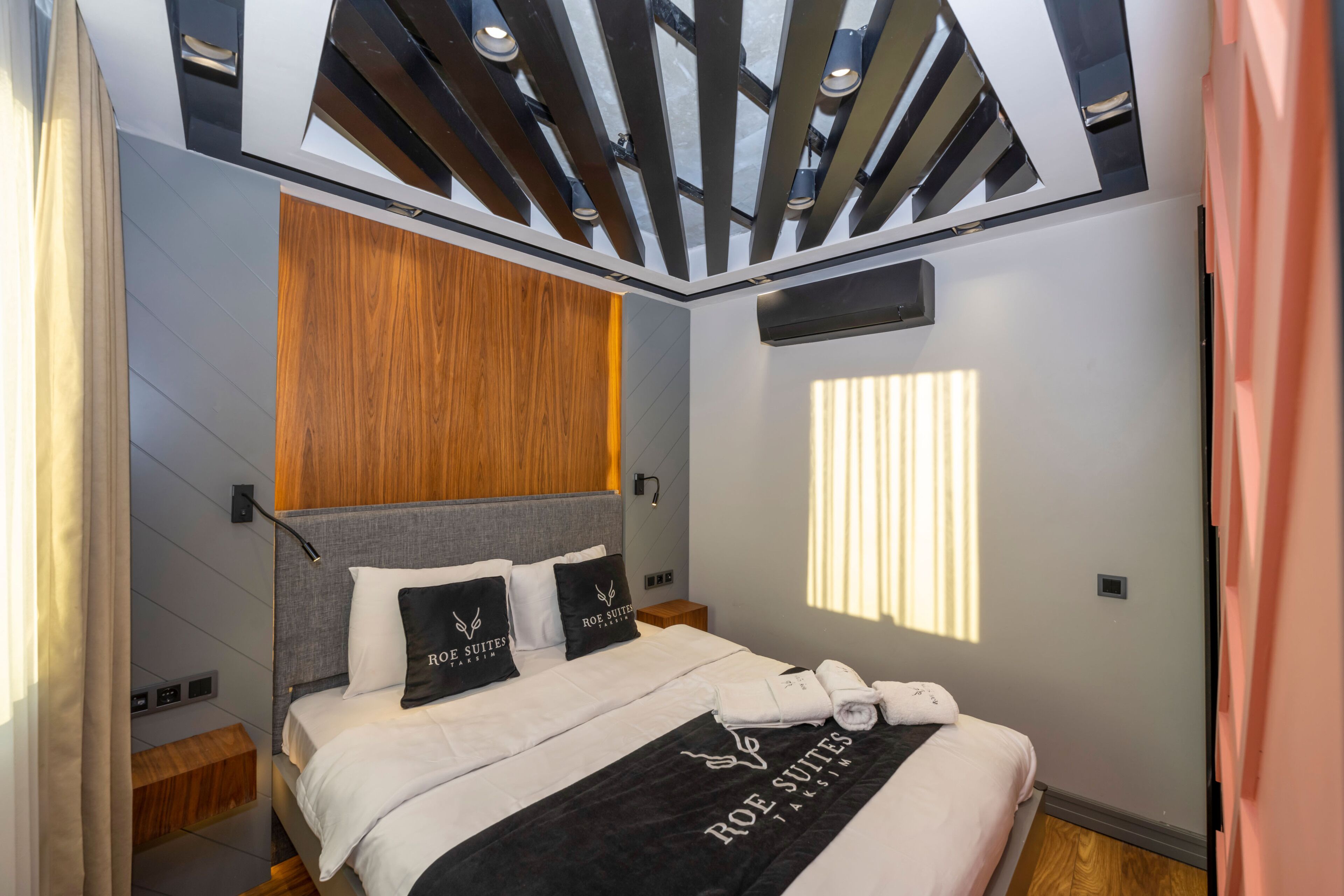 A modern bedroom with a bed, wooden headboard, and a skylight.