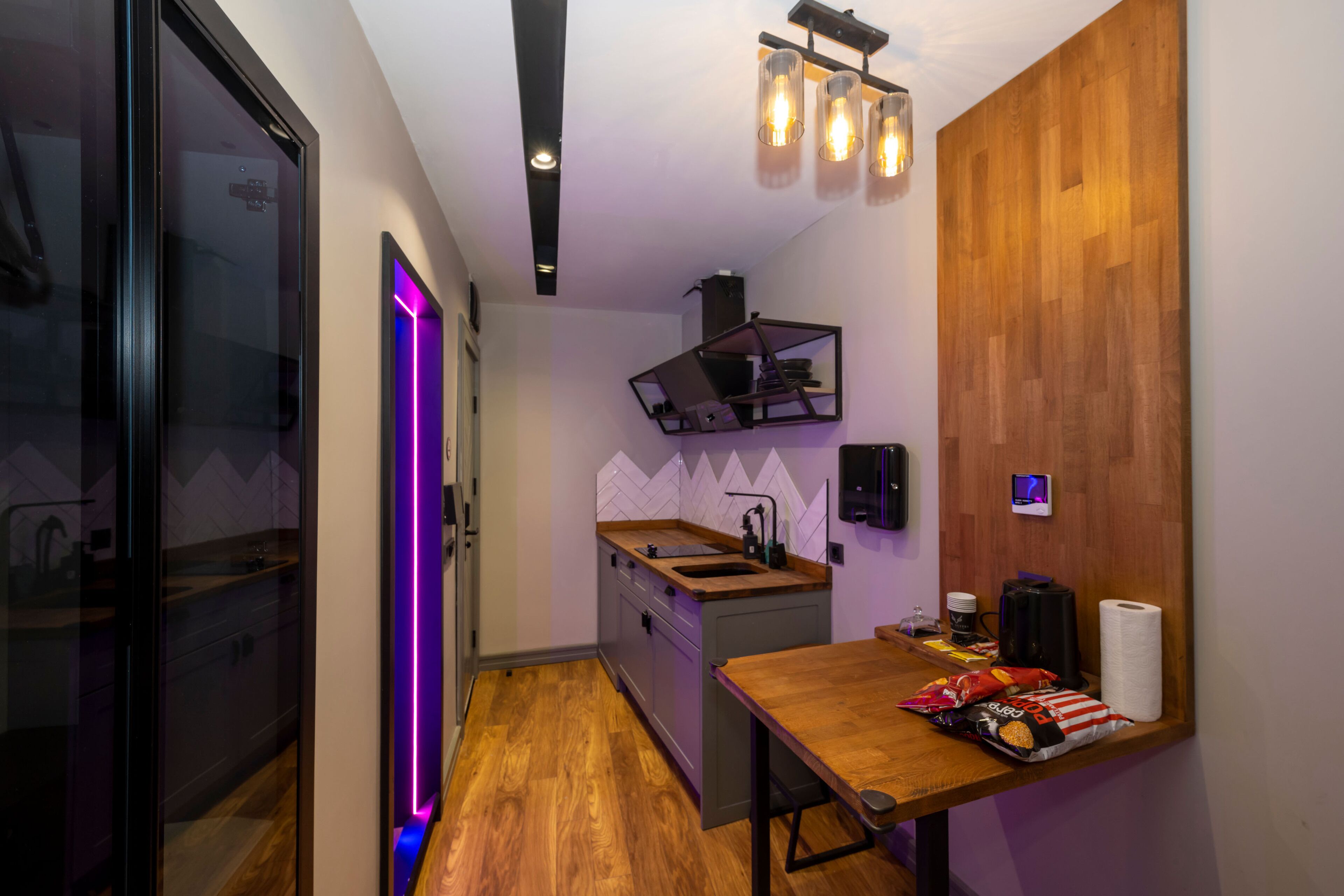 A compact kitchen with a wooden countertop, a sink, and a small island. There is a wooden wall panel and a ceiling light fixture.