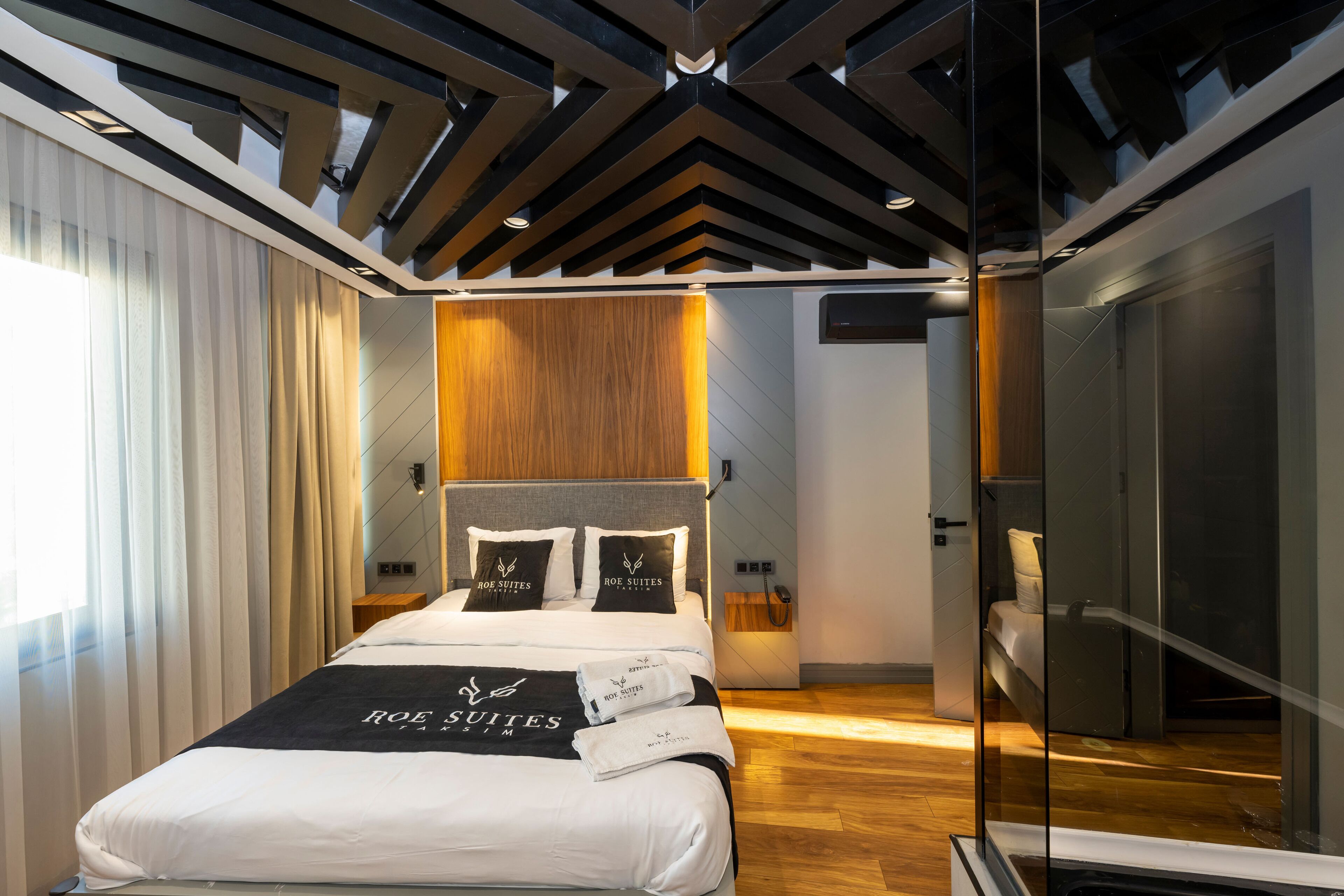 A modern hotel room with a large bed, wooden headboard, and a glass partition.