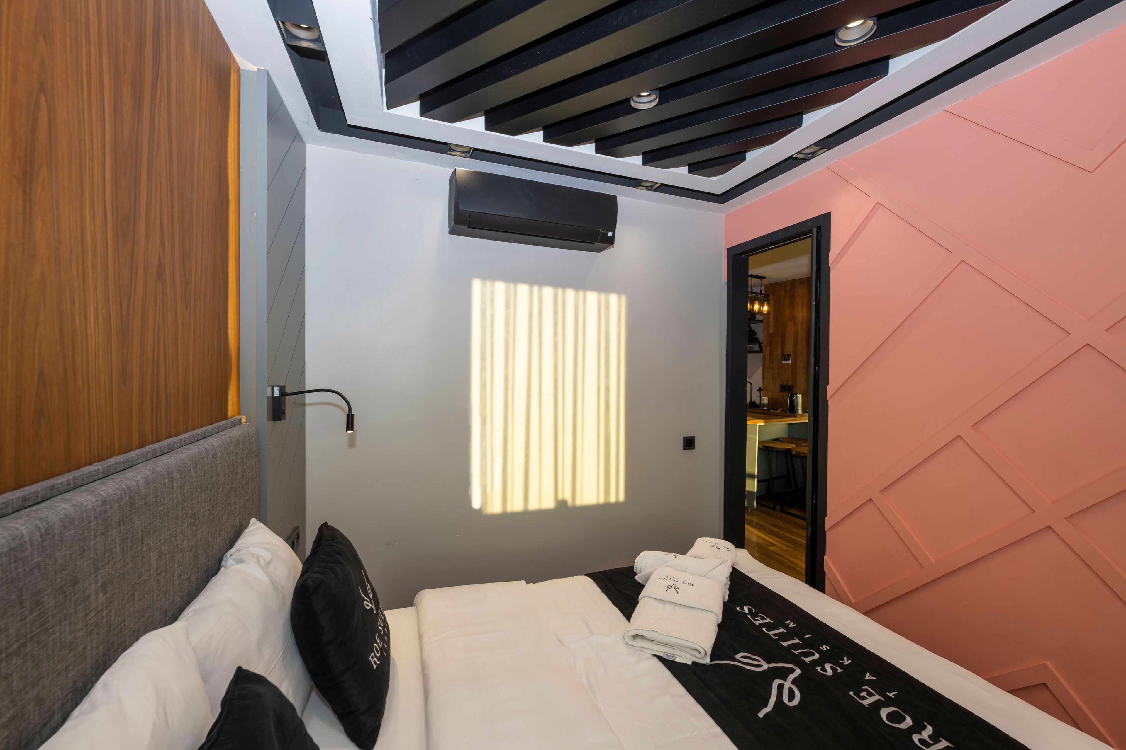 Una habitación de hotel moderna con una cama, un armario de madera, un techo con luz empotrada y una pared decorada en color rosa.