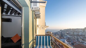 Ein Balkon mit einem gestreiften Stuhl, einer Couch und Blick auf eine Stadtansicht.
