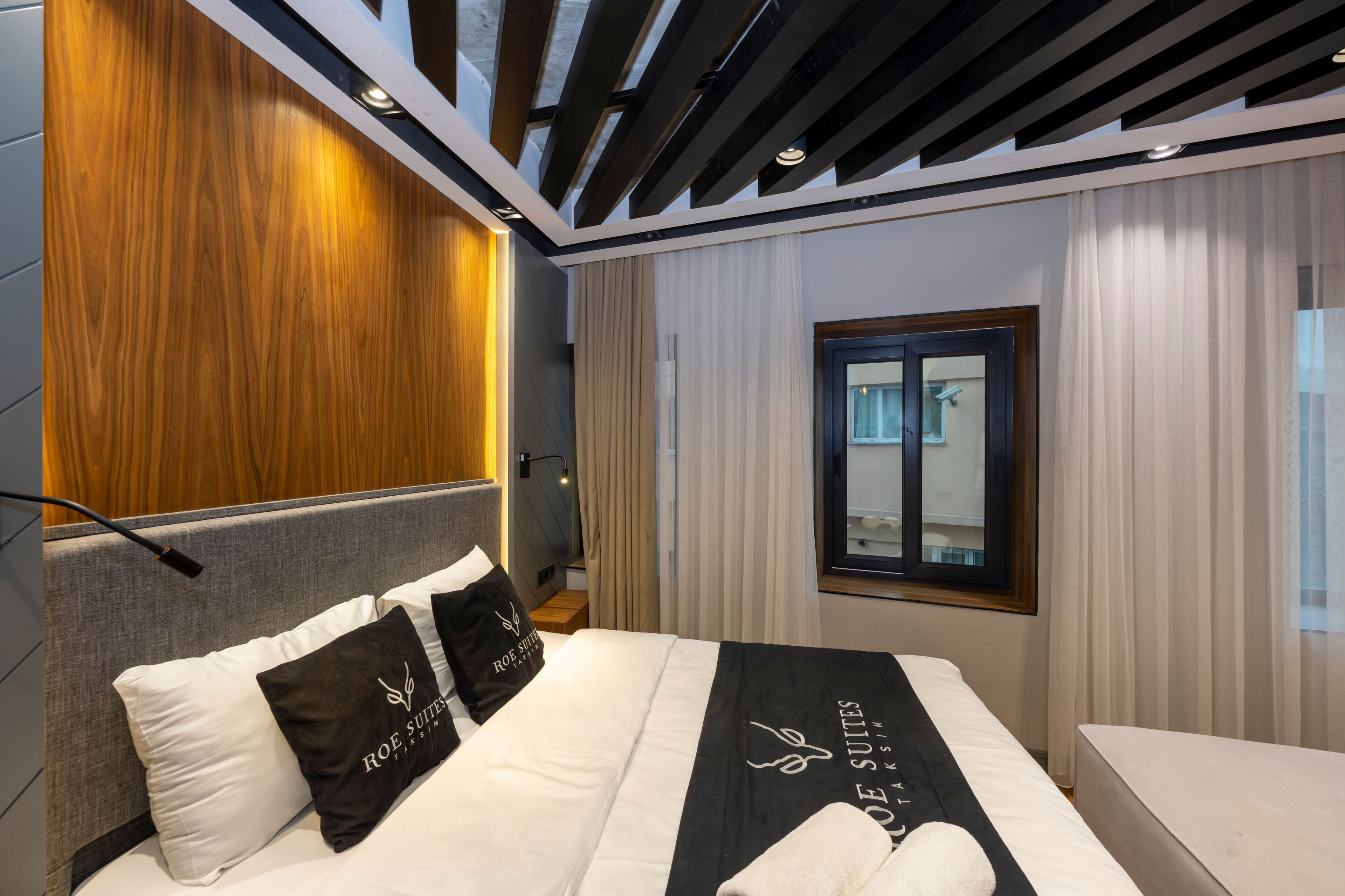 A modern hotel room with a bed, a window, and a wooden accent wall.