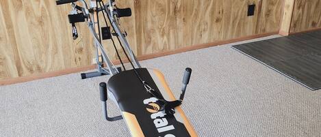 A gym with a bench and exercise equipment against a wooden wall.