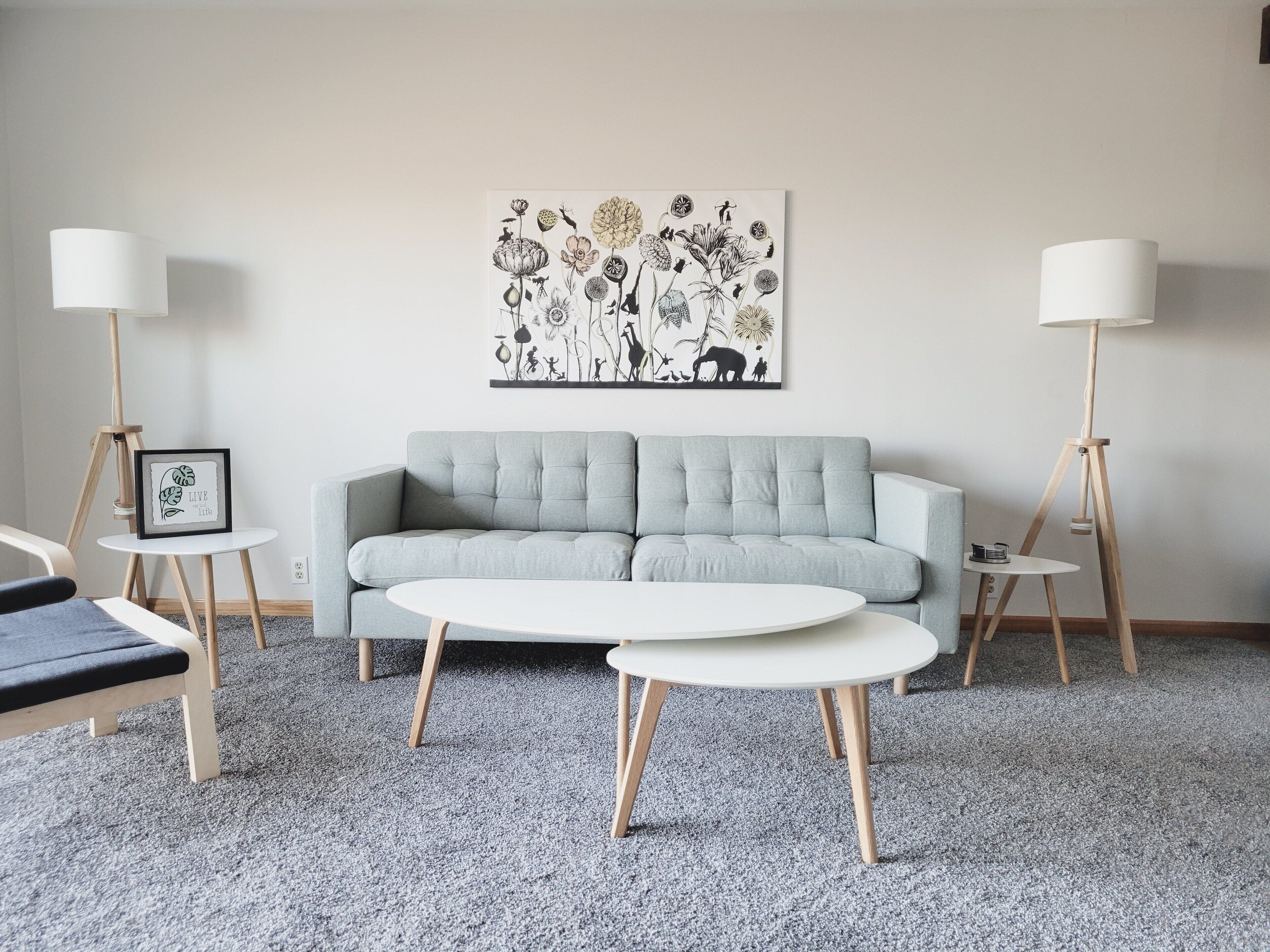 Un salon moderne avec un canapé gris, deux petites tables rondes blanches et deux lampadaires.