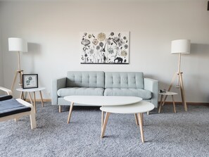 A modern living room with a grey sofa, two white round tables, and two floor lamps.
