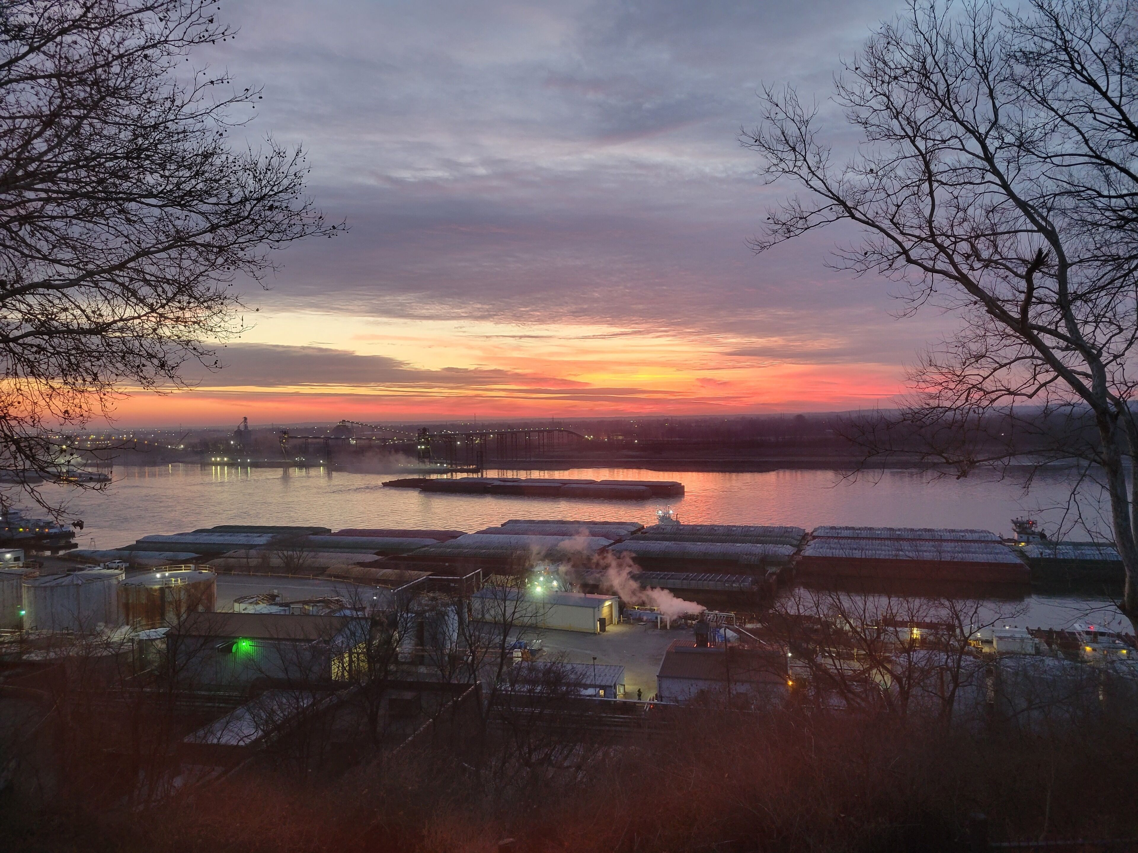 A riverside industrial area with buildings and structures along the water, including a dock and a large water tower.