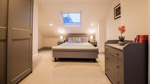 Un dormitorio con cama, lámparas de noche, mesita de noche, cómoda, ventana y una planta pequeña.