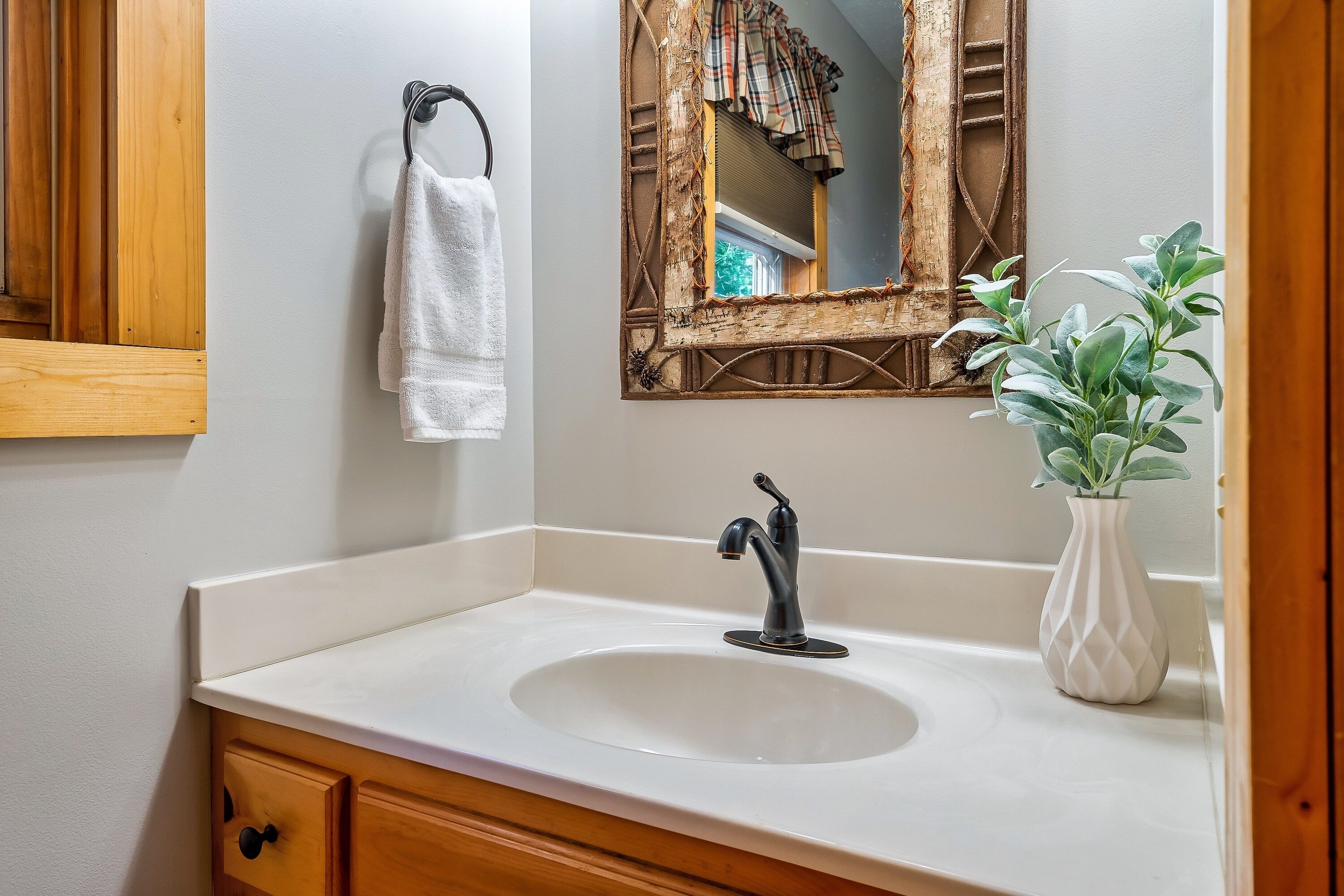 A bathroom with a white sink, a wooden vanity, a mirror with a rustic frame, and a potted plant.