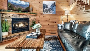 A cozy living room with a stone fireplace, a wooden coffee table, a leather sofa, and a large painting of a bear.