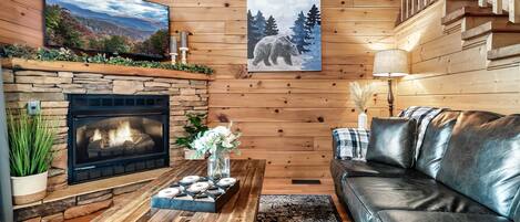 A cozy living room with a stone fireplace, a wooden coffee table, a leather sofa, and a large painting of a bear.