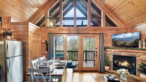 A wooden cabin interior with a dining area, a fireplace, and a view of the outdoors.