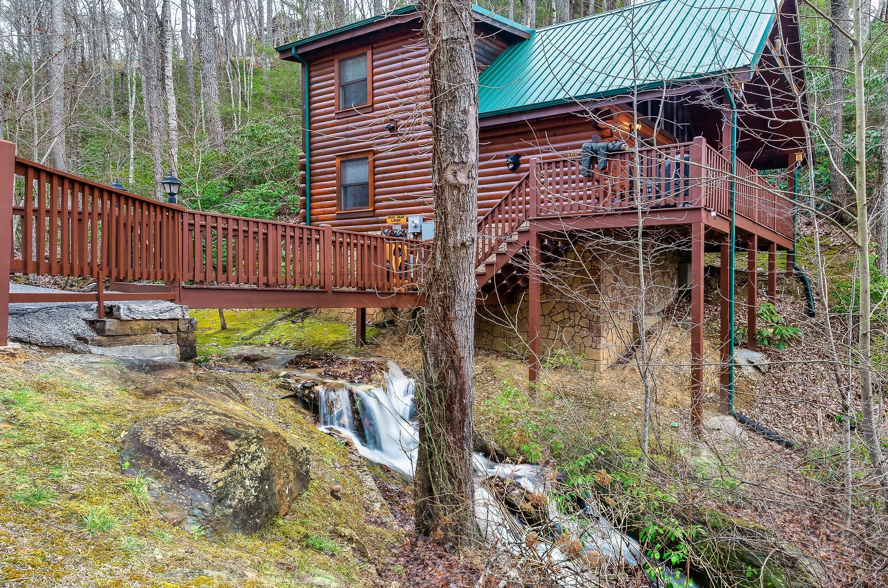 A rustic cabin with a wooden deck and a small waterfall.