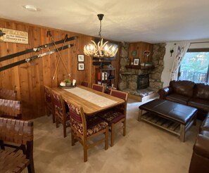 L’intérieur d’un chalet accueillant, avec une table à manger en bois, des chaises, une cheminée, un canapé en cuir et un mur en pierre.