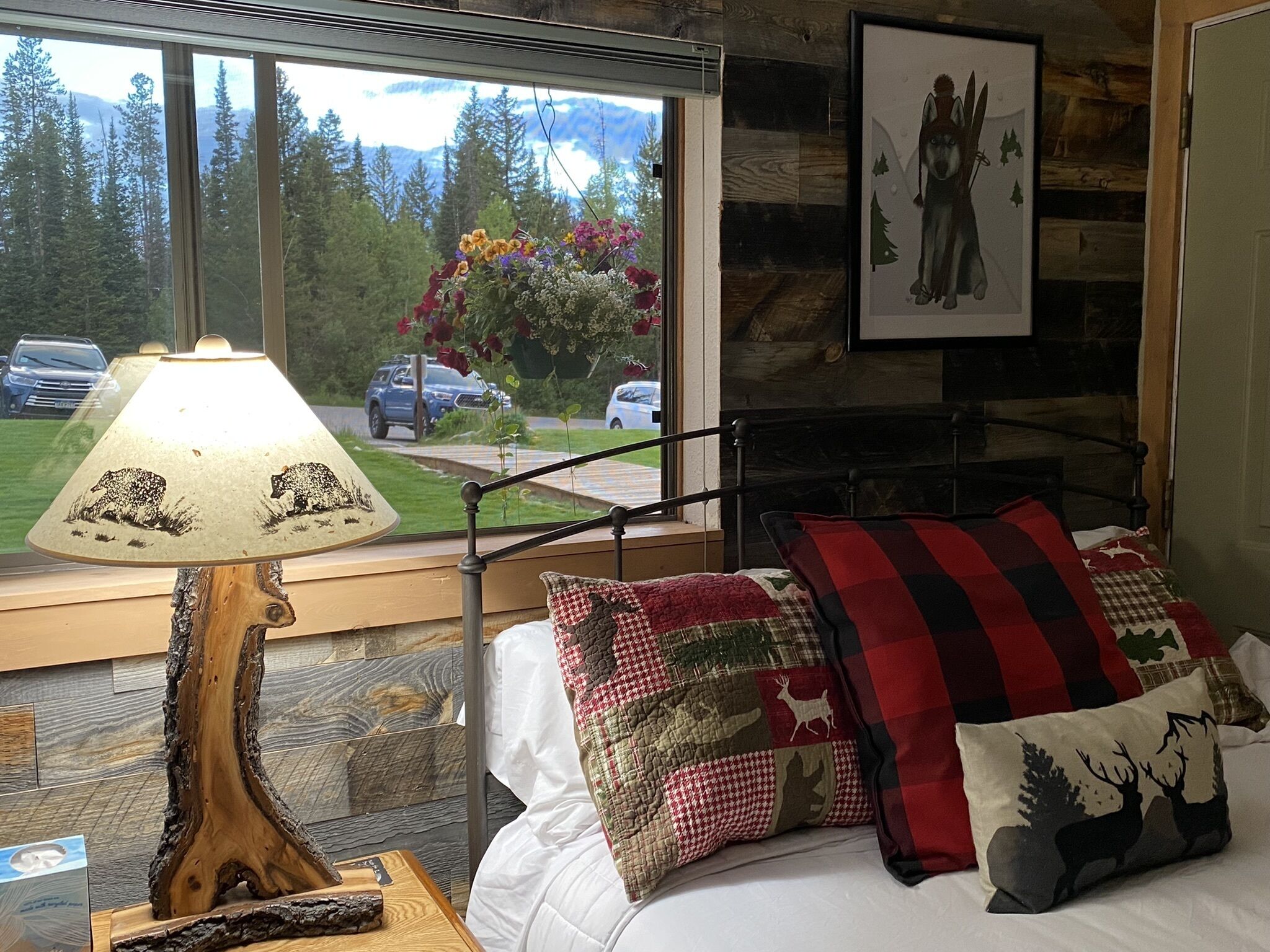 A bedroom with a bed, a lamp, and a window with a view of a forest and mountains.