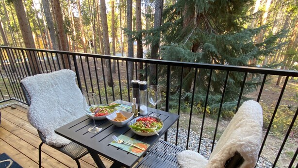 Een eettafel met een glas wijn, twee saladekommen en een waterfles op een balkon met een reling.