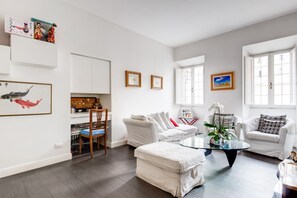 A modern living room with a white sofa, a glass coffee table, and a dining area with a wooden chair.