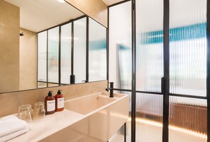 Ein modernes Badezimmer mit einem großen Spiegel, einem beige farbenen Waschbecken und zwei Shampoo-Flaschen.