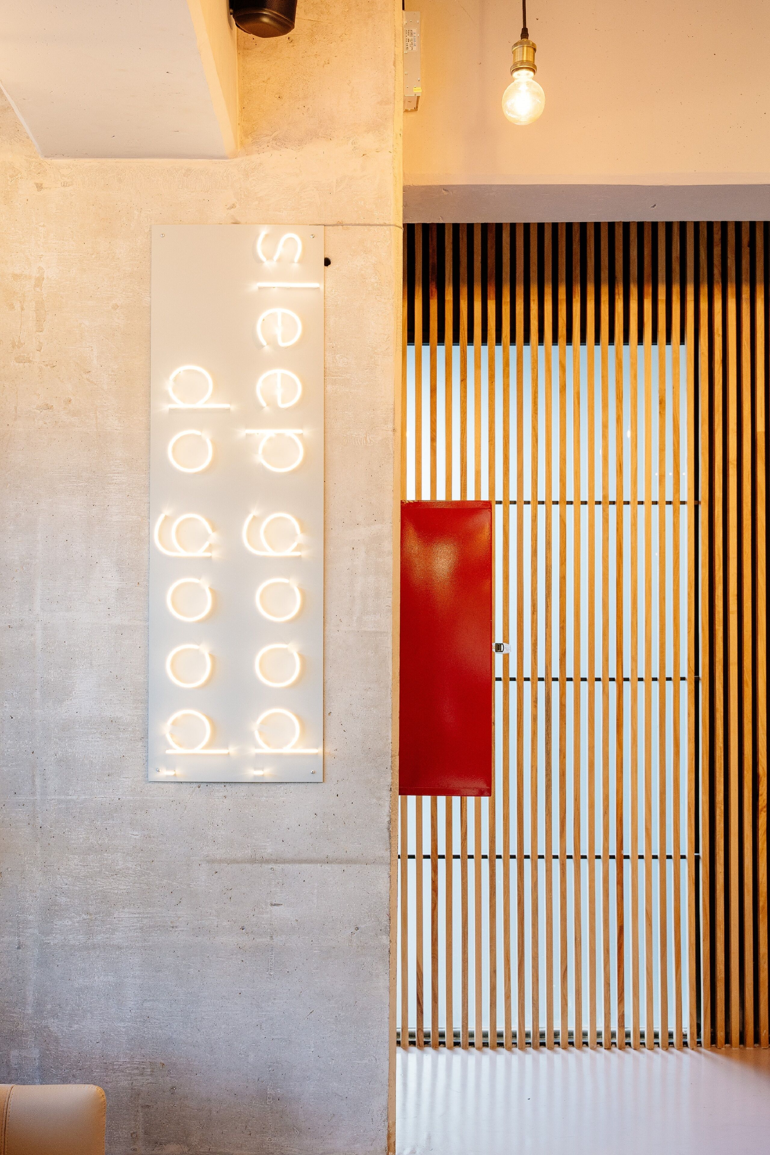 Une pièce avec un mur en béton, un panneau décoratif rouge et une cloison en bois à lattes.
