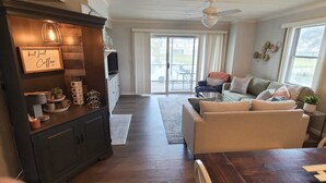 Ein geräumiges Wohnzimmer mit einem dunklen Holzschrank, einem Flachbildfernseher und einem großen Fenster mit Blick ins Freie.