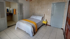 Un dormitorio con una cama, un muro con patrón de ladrillo, una puerta y piso de baldosas.