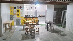 Un comedor con mesas y sillas, una cocina al fondo y piso de baldosas.