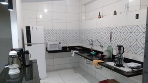 Una cocina moderna con azulejos blancos, encimera negra, microondas, hervidor y cafetera.