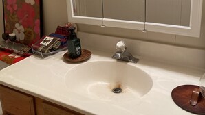 Un baño con lavamanos blanco, armarios de madera, un espejo y una obra de arte floral en la pared.