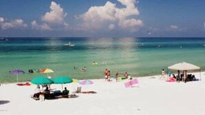 Ein Strand mit klarem, türkisfarbenem Wasser, ein paar Schwimmer und bunte Sonnenschirme im Sand.