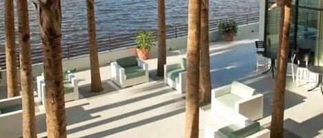 Una terraza con mobiliario exterior blanco, palmeras y vista al mar.