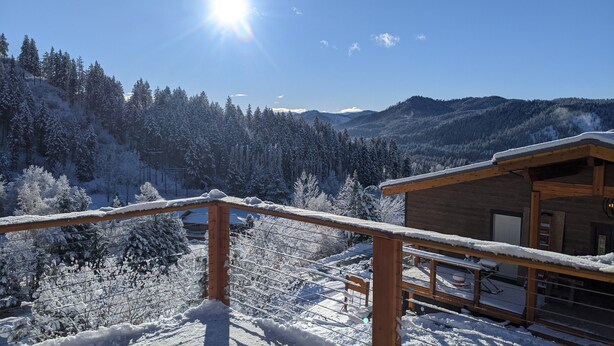 Uma cabana de madeira com varanda com vista para uma paisagem montanhosa coberta de neve.
