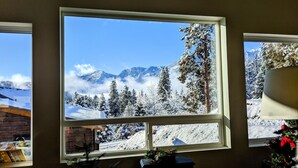 Uma janela com vista para montanhas e árvores cobertas de neve.