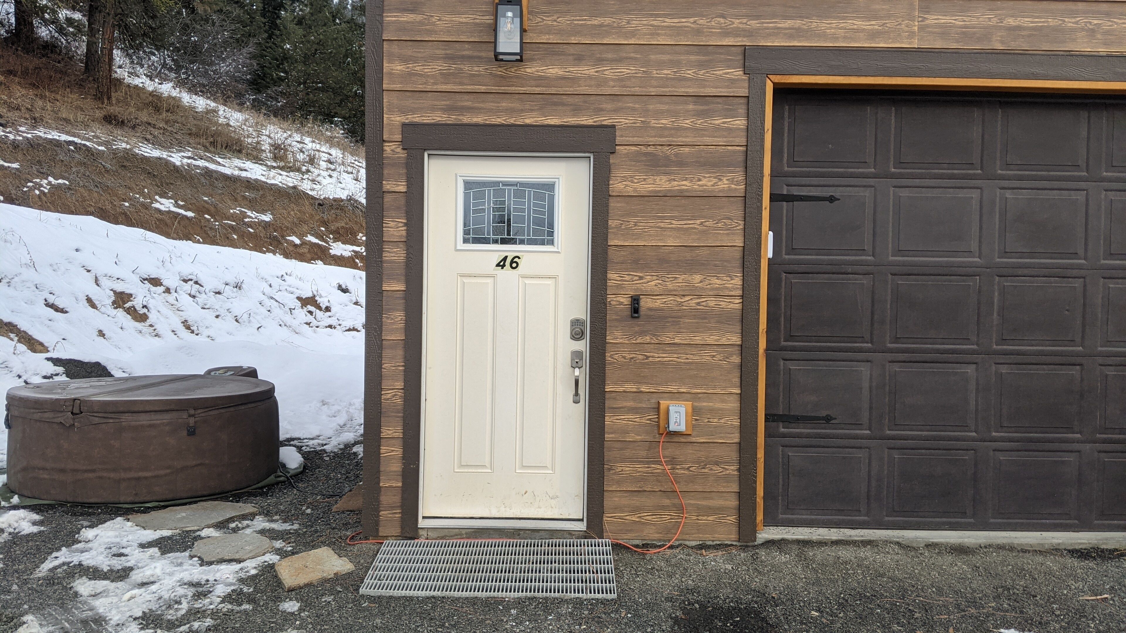 A building with a white door marked with the number 46, a brown garage door, and a large brown water heater outside.