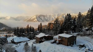 Um conjunto de cabanas com vários edifícios, rodeado por árvores cobertas de neve e montanhas ao fundo.