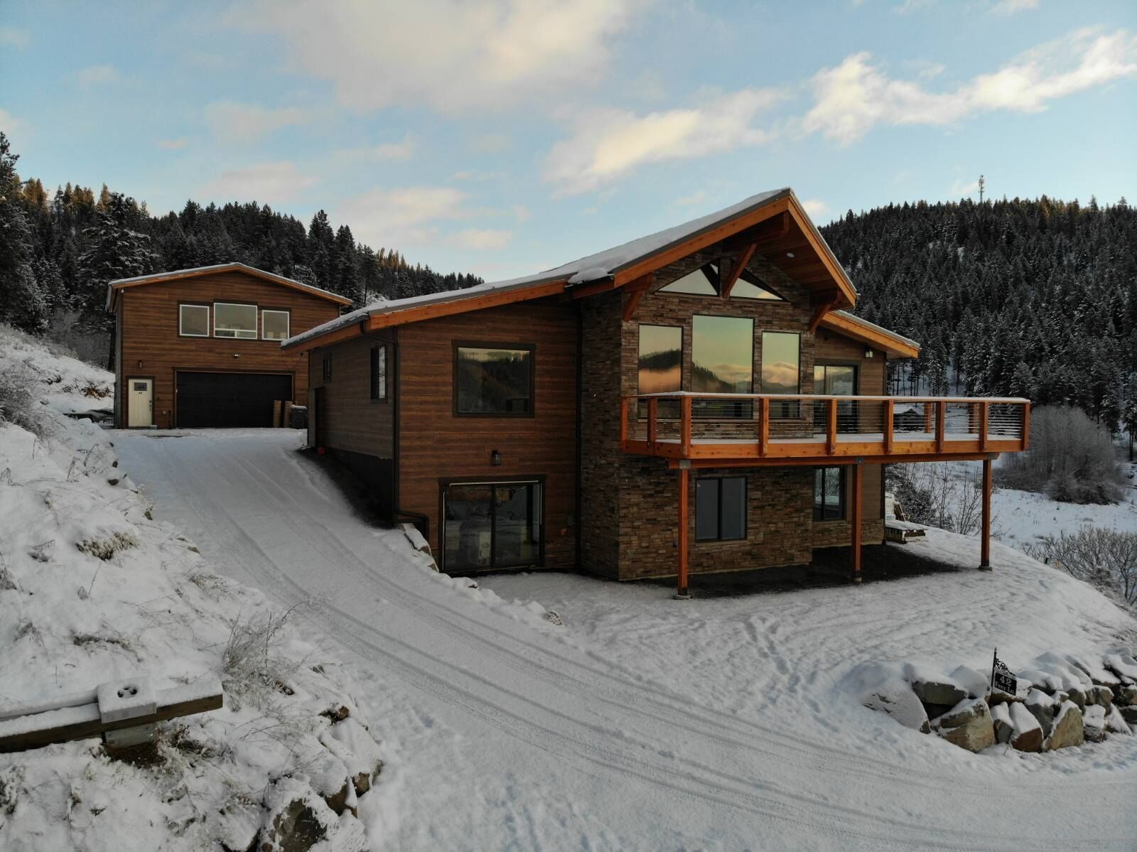 Une cabane en bois à deux étages, dotée d’un balcon, entourée d’un paysage enneigé et d’une forêt.