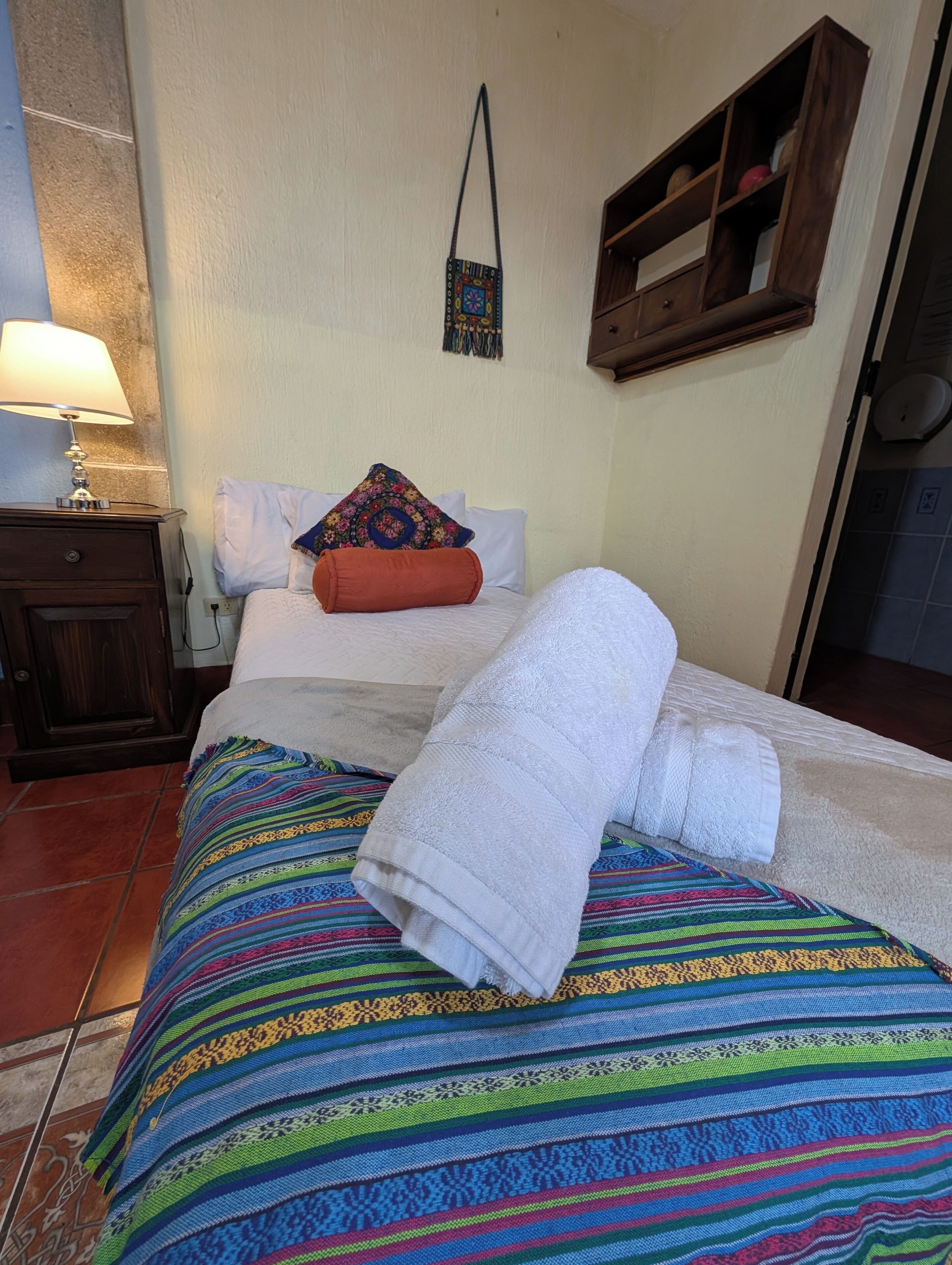 Una cama bien hecha con un edredón colorido, una toalla blanca y una almohada decorativa.