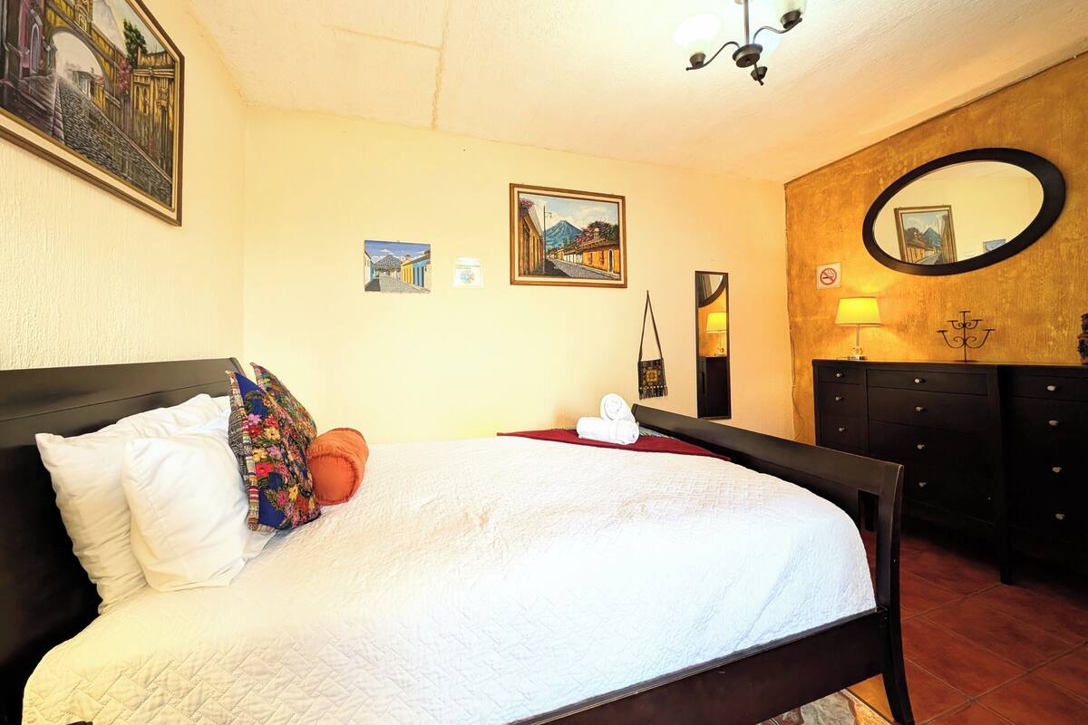 Une chambre d’hôtel avec un lit, un miroir fixé au mur et un luminaire au plafond.