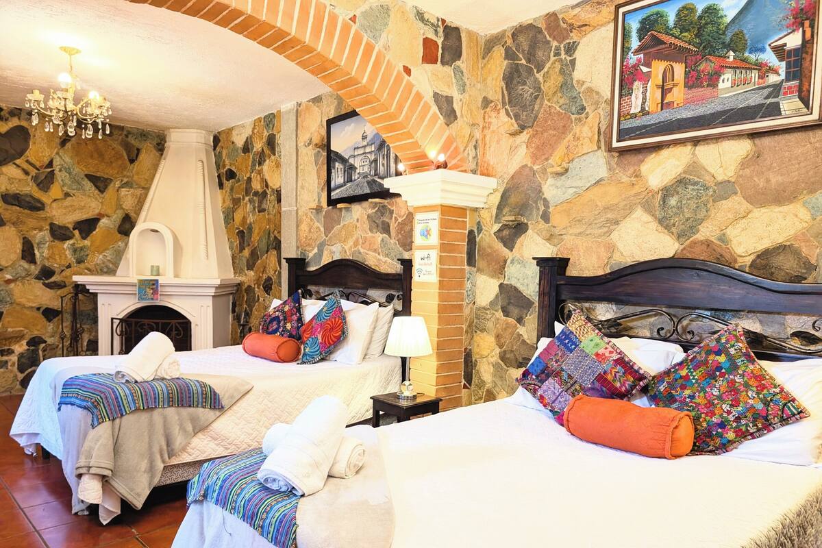 Une chambre d’hôtel avec deux lits, des murs en pierre, une cheminée et un lustre.