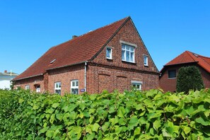 Ein zweistöckiges Backsteinhaus mit rotem Ziegeldach, umgeben von üppigem Grün.
