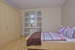Un dormitorio con cama, armario, ventana con cortinas y radiador.