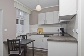 A compact kitchen with white cabinets, a wooden countertop, a built-in oven, and a dining area with a table and chairs. - F-1009 Sonnenhut - Ferienwohnung Sonnenhut F-1009 (Baabe)