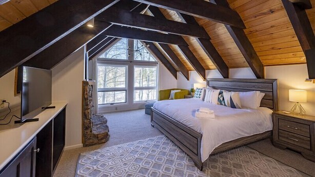 Een slaapkamer met een schuine kap, een groot bed, een televisie en een stenen muur.