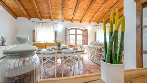 A dining area with a wooden ceiling, a white table with chairs, and a window with curtains. - Domos Pintadas Cottage Rosa (Olbia)